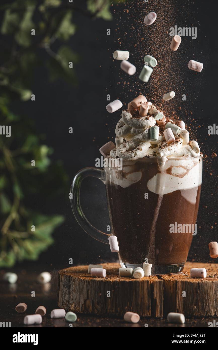 Marshmallow e cacao in polvere cadono su una tazza di cioccolata calda e panna montata su un asse di legno in un'atmosfera accogliente Foto Stock Marshmallow e cacao in polvere cadono su una tazza di cioccolata calda e panna montata su un asse di legno in un'atmosfera accogliente Foto Stock