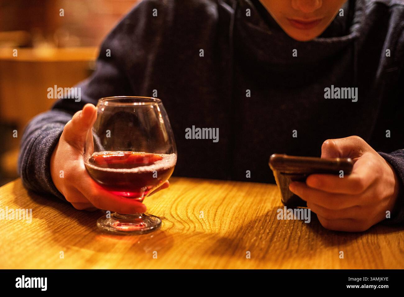 bevi il tè alla frutta da un calice di vetro e guardalo su uno smartphone. Pranzo Foto Stock