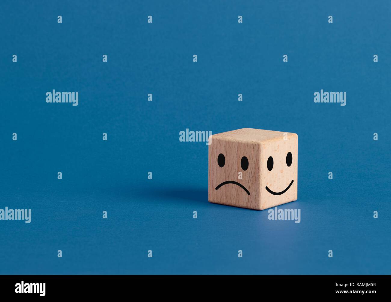 Cubo di legno che mostra sia un volto felice che triste rappresenta la dualità dei sentimenti e l'ambivalenza emotiva. Esperienza del cliente, del cliente o dell'utente. Foto Stock