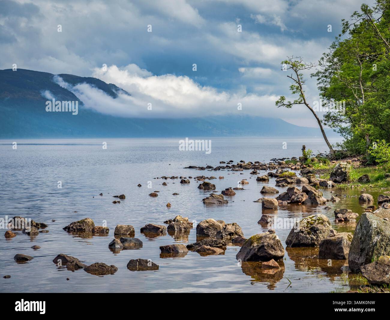 Il sole sulla riva orientale del Loch Ness nelle Highlands scozzesi, mentre le nuvole si infrangono sulle colline sulla riva occidentale. Foto Stock