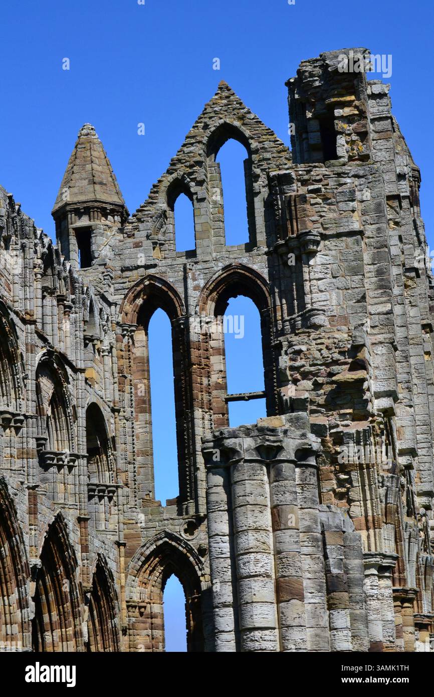 Primo piano delle rovine gotiche di Whitby Abbey a Whitby, North Yorkshire, Regno Unito, con intricati lavori in pietra e archi su un cielo azzurro. 🏰✨ Foto Stock