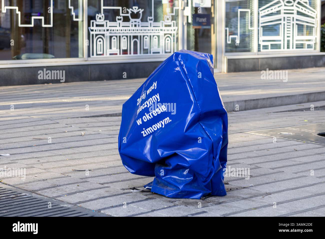 Copertura blu sopra una fontana pubblica di acqua potabile con cartelli stagionali in polacco che indicano la chiusura invernale, collocata su un marciapiede urbano di fronte Foto Stock