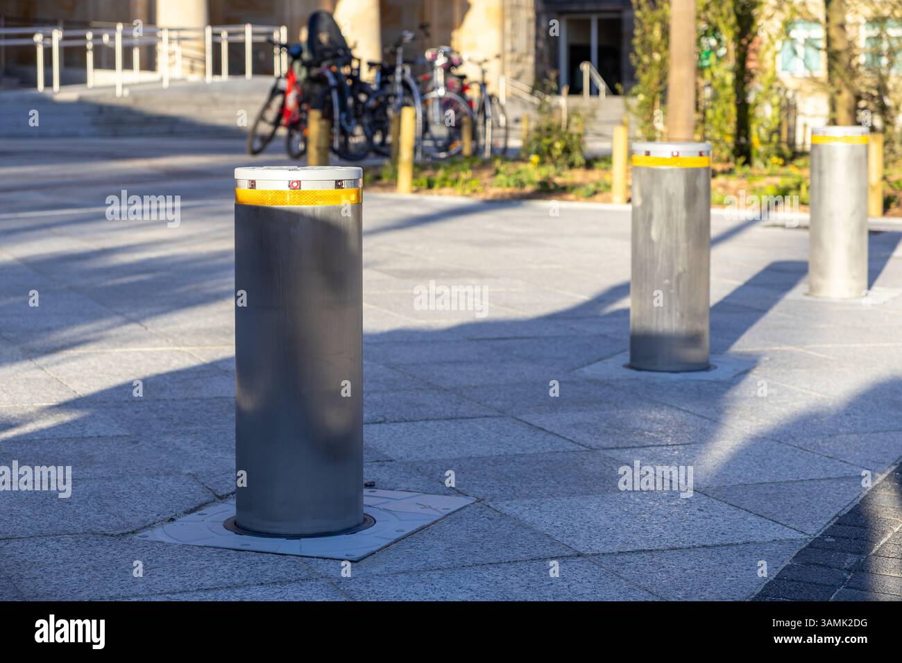 Robusti dissuasori in metallo con bande riflettenti installati in una moderna piazza della città per controllare l'accesso al veicolo, visti alla luce del sole con biciclette e archi Foto Stock