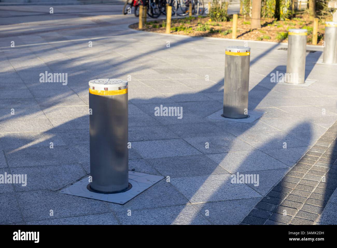 I dissuasori in metallo sono incorporati nei marciapiedi urbani piastrellati, riflettendo la luce del mattino e le ombre, progettati per limitare l'accesso al veicolo ed e Foto Stock