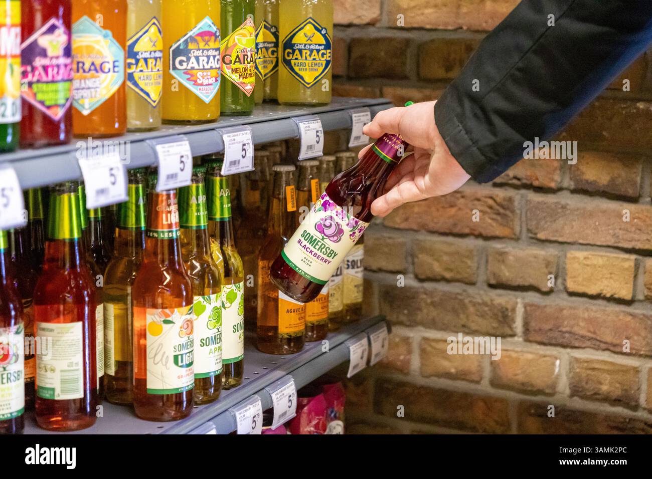 Poznan, Polonia - 8 aprile 2025: Primo piano di una mano che raccoglie una bottiglia di sidro di mora di Somersby da uno scaffale del negozio tra varie bevande aromatizzate, berretto Foto Stock