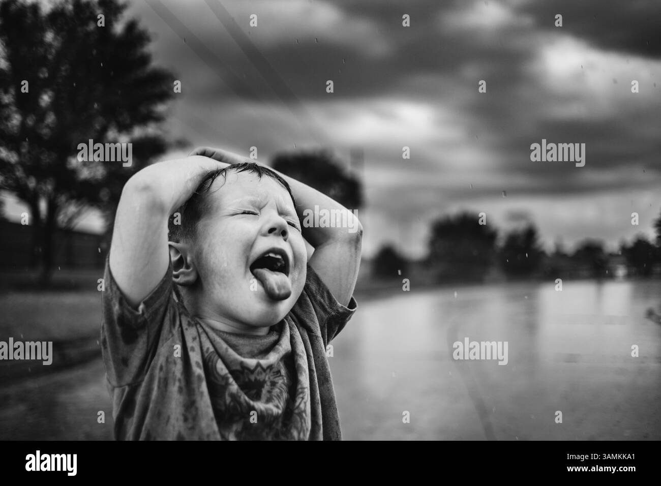 Black and White Boy che guarda in alto catturando gocce d'pioggia in bocca Foto Stock