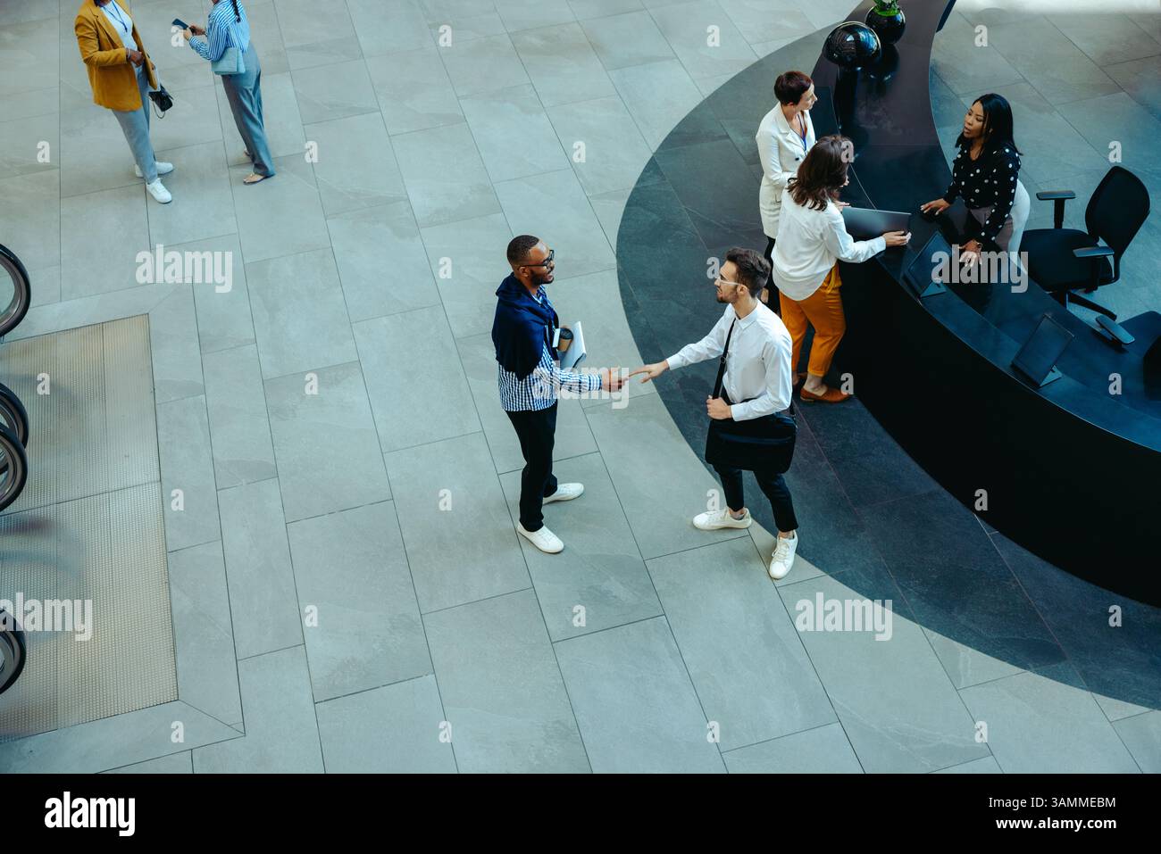 Vista dall'alto dei colleghi che stringono la mano in una lobby aziendale, illustrando il saluto professionale, il lavoro di squadra e l'avanzamento di carriera. Foto Stock