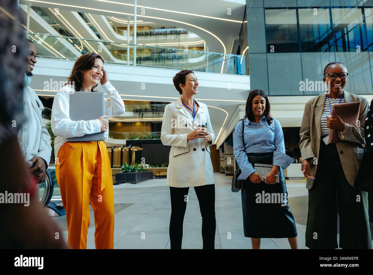 Un gruppo variegato di professionisti si riunisce in una moderna lobby di uffici per una riunione informale. Le loro espressioni mostrano coinvolgimento e collaborazione, riflessioni Foto Stock
