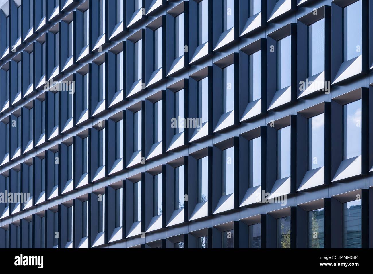 Facciata moderna e ripetitiva di un edificio di uffici con finestre rettangolari che creano un motivo geometrico astratto, sfondo con struttura architettonica a luce naturale Foto Stock