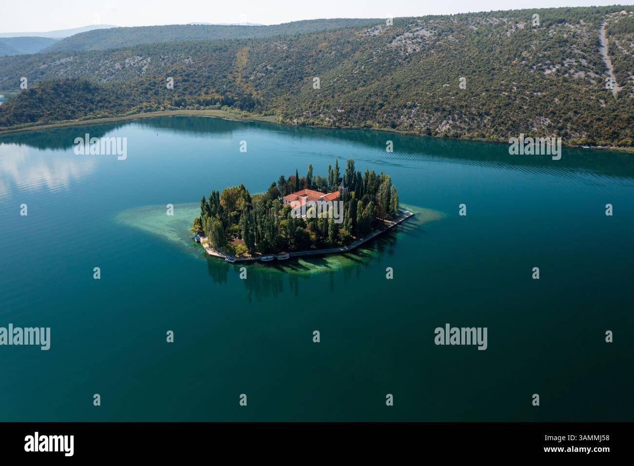 Vista aerea di un'isola tranquilla e pittoresca circondata da un lago tranquillo e da una foresta lussureggiante, Drnis, Croazia. Foto Stock