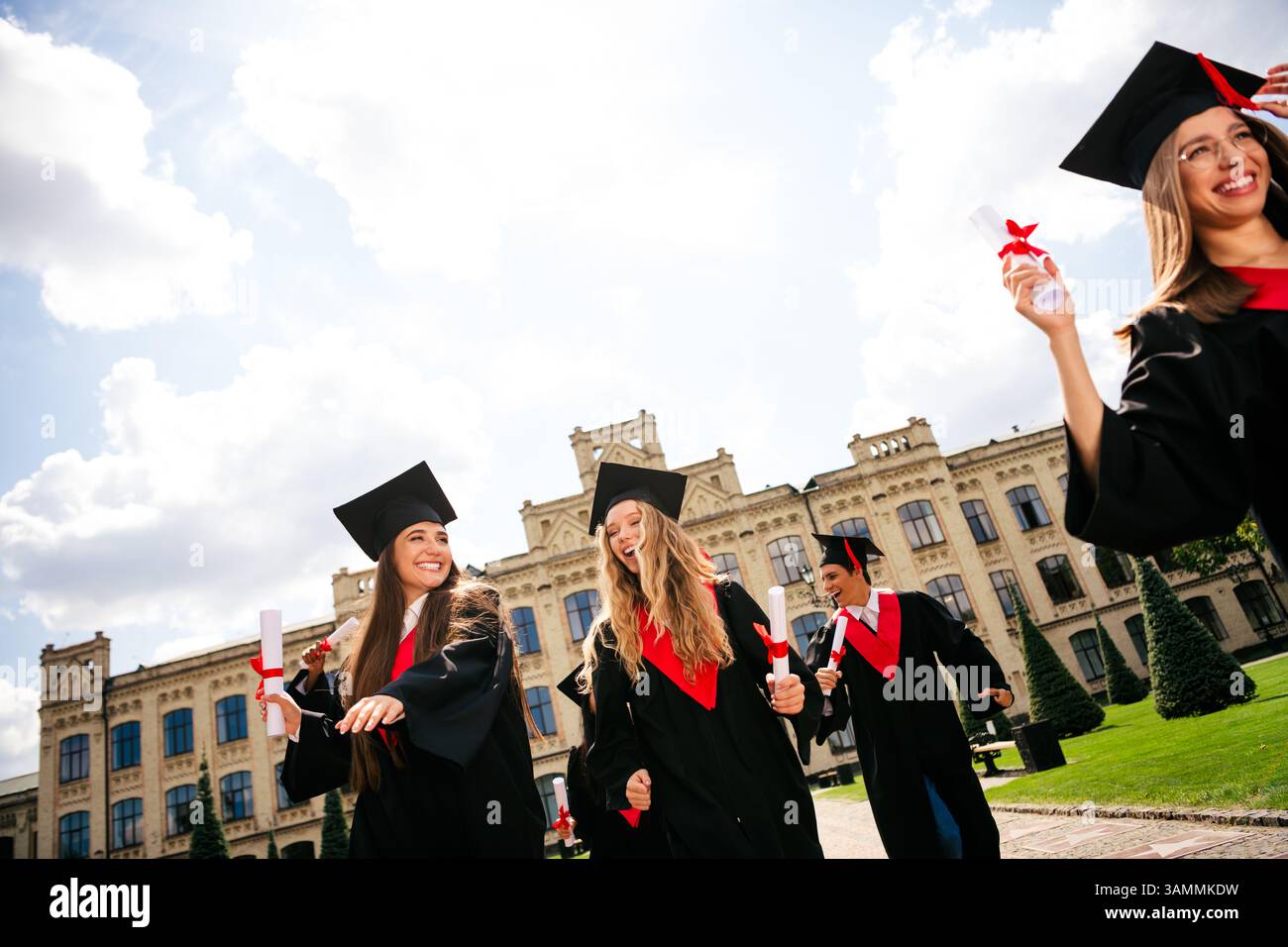 Allegri laureati che festeggiano all'aperto in abiti e bacheche con diplomi in uno splendido campus universitario in una giornata di sole Foto Stock