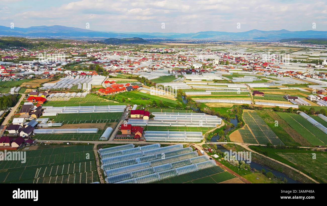 Vista aerea delle fattorie e del villaggio serra. Ampia vista aerea delle fattorie a effetto serra, dei campi coltivati e di un piccolo villaggio circondato da montagne Foto Stock