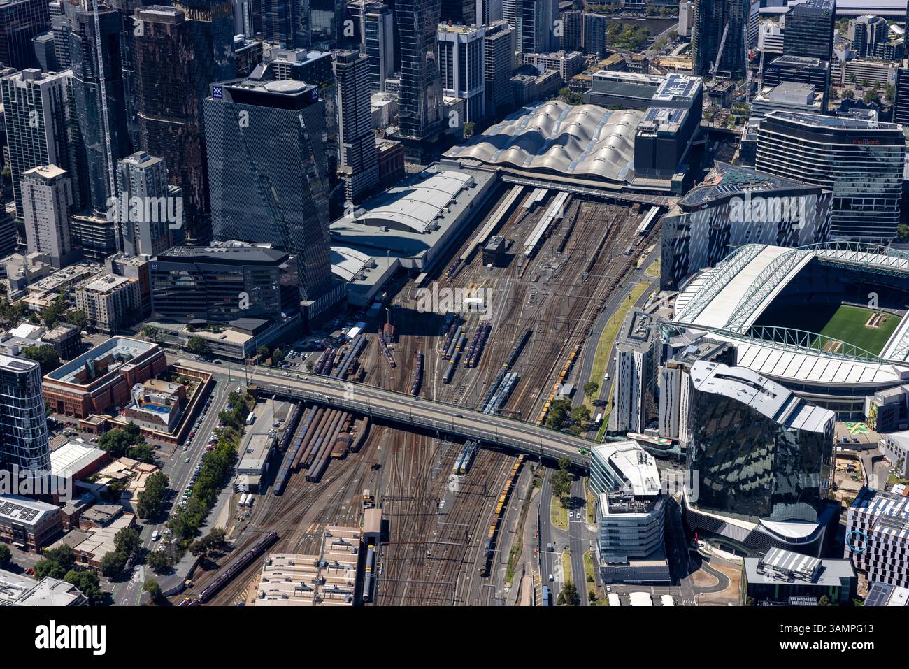 Veduta aerea della trafficata stazione ferroviaria e dei binari tra edifici moderni e uno stadio, West Melbourne, Australia. Foto Stock