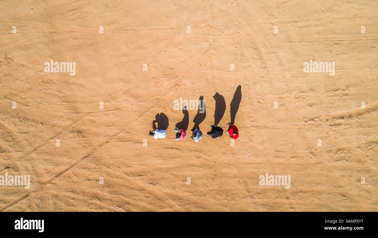 Vista aerea di amici che imitano l'evoluzione umana con le loro ombre nel deserto di Sharjah, U.A.E. Foto Stock