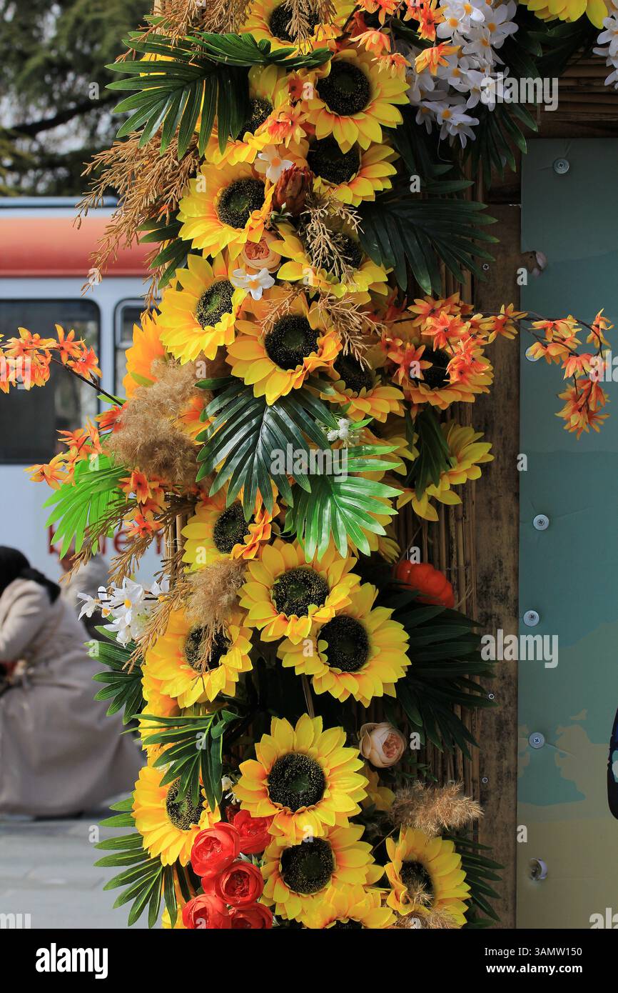 Fiori di plastica in vari colori. Girasoli e foglie gialle. Foto Stock
