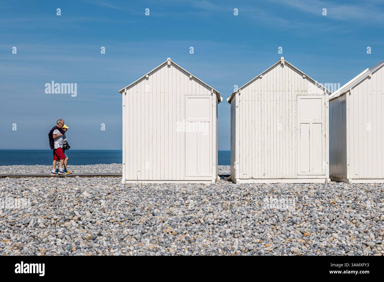 Cayeux-sur-Mer (Francia settentrionale): Rifugi e due turisti sulla passerella in legno "chemin des Planches" lungo la spiaggia di ciottoli Foto Stock