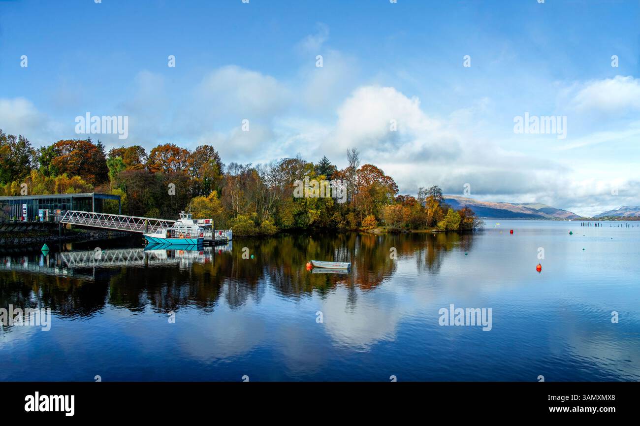 Una vista del lago con la luce del sole sulle foglie autunnali sul lato del lago Lomond in Scozia. Mostra le barche accanto al molo di Balloch. Foto Stock