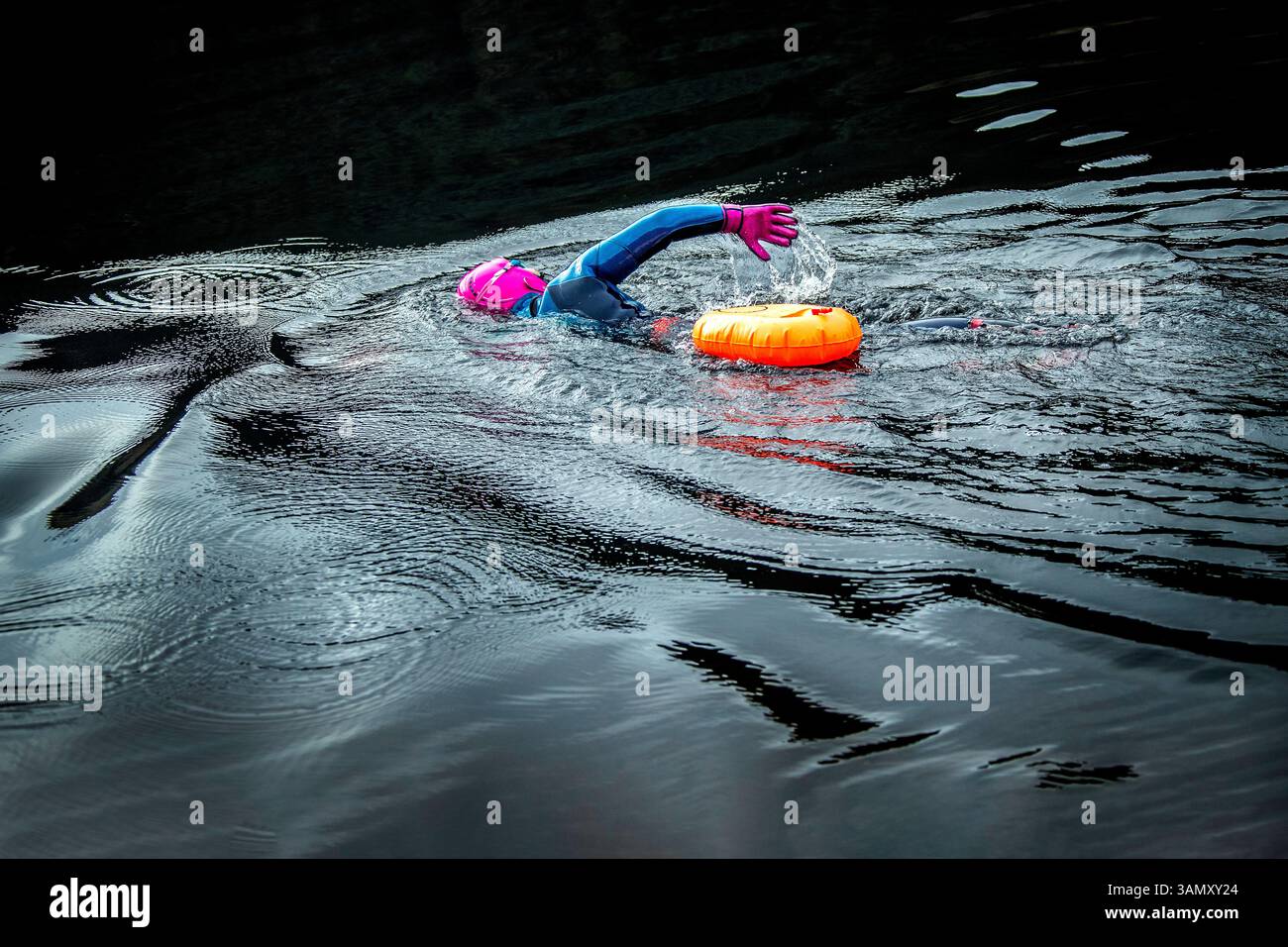Vista laterale del bagnino con guanti rosa brillante e casco nelle acque fredde e scure del lago. Foto Stock