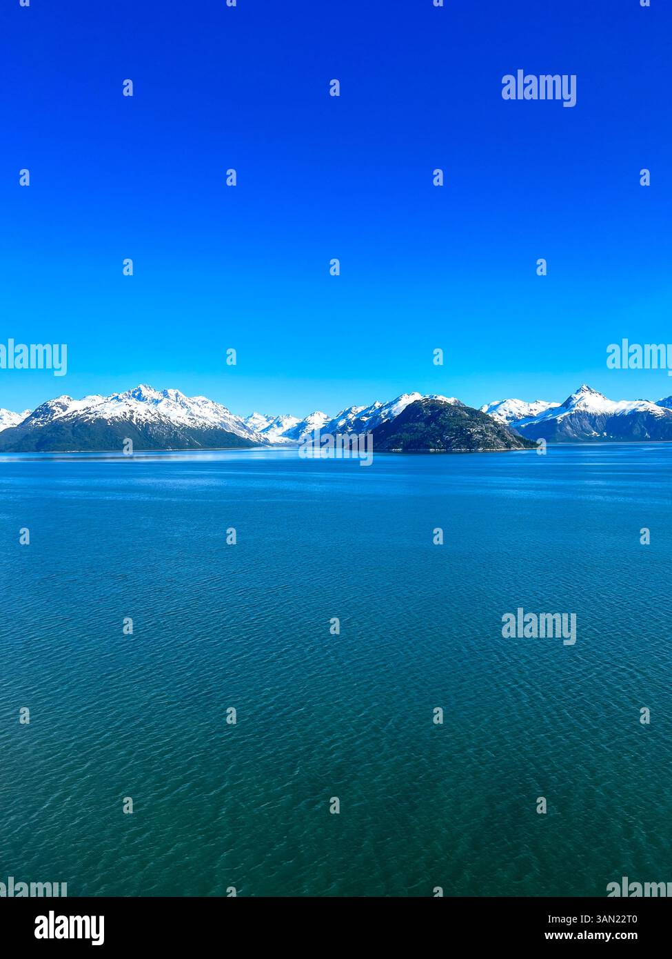 Una splendida vista di Glacier Bay, Alaska, con le sue acque blu, le montagne innevate e un'isola tranquilla sotto un cielo limpido. Una biglia perfetta - Immagine stock catturata con smartphone