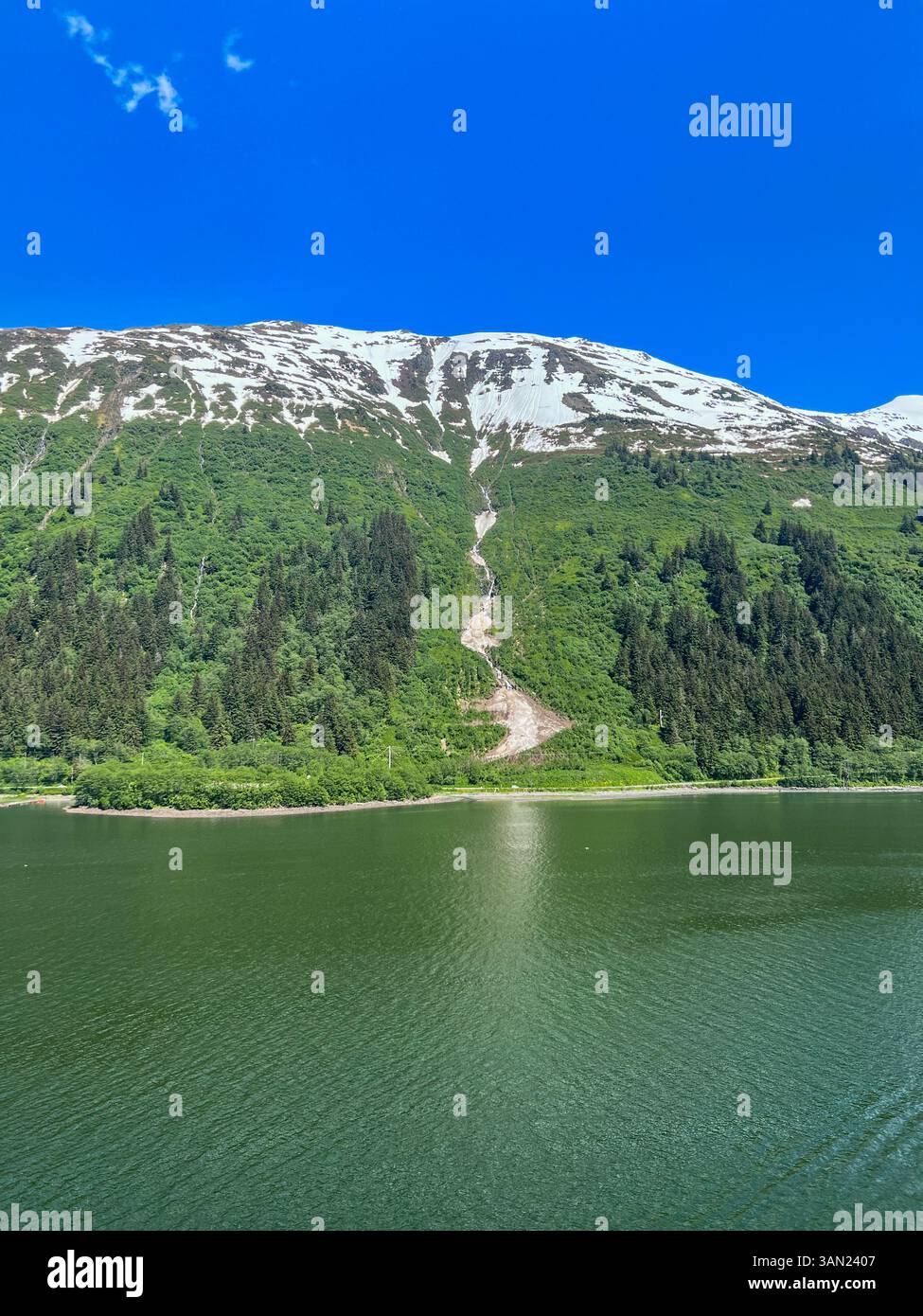 Una splendida vista sulle lussureggianti montagne verdi dell'Alaska, una cascata e i resti ghiacciati della neve che si fondono nelle acque incontaminate sottostanti. Catturato - Immagine stock catturata con smartphone