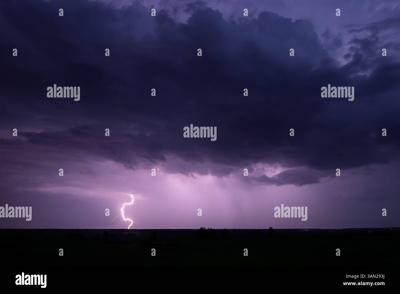 Un potente fulmine attraversa il cielo notturno durante un temporale, proiettando un bagliore viola sul paesaggio. Foto Stock