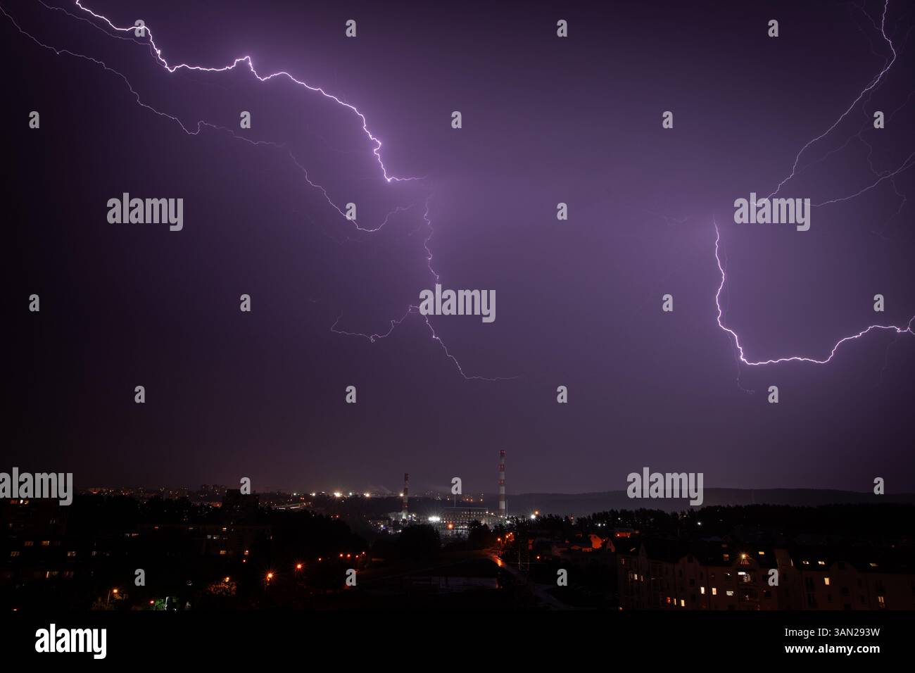 I fulmini spettacolari si estendono attraverso il cielo notturno sopra un lontano paesaggio urbano, proiettando un'inquietante bagliore viola sugli edifici sottostanti. Foto Stock