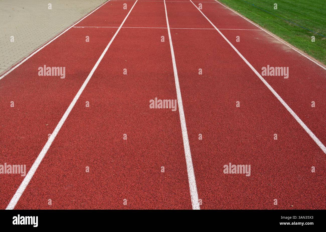 Pista da corsa rossa con linee bianche, sentiero sul lato sinistro e erba verde sul lato destro Foto Stock