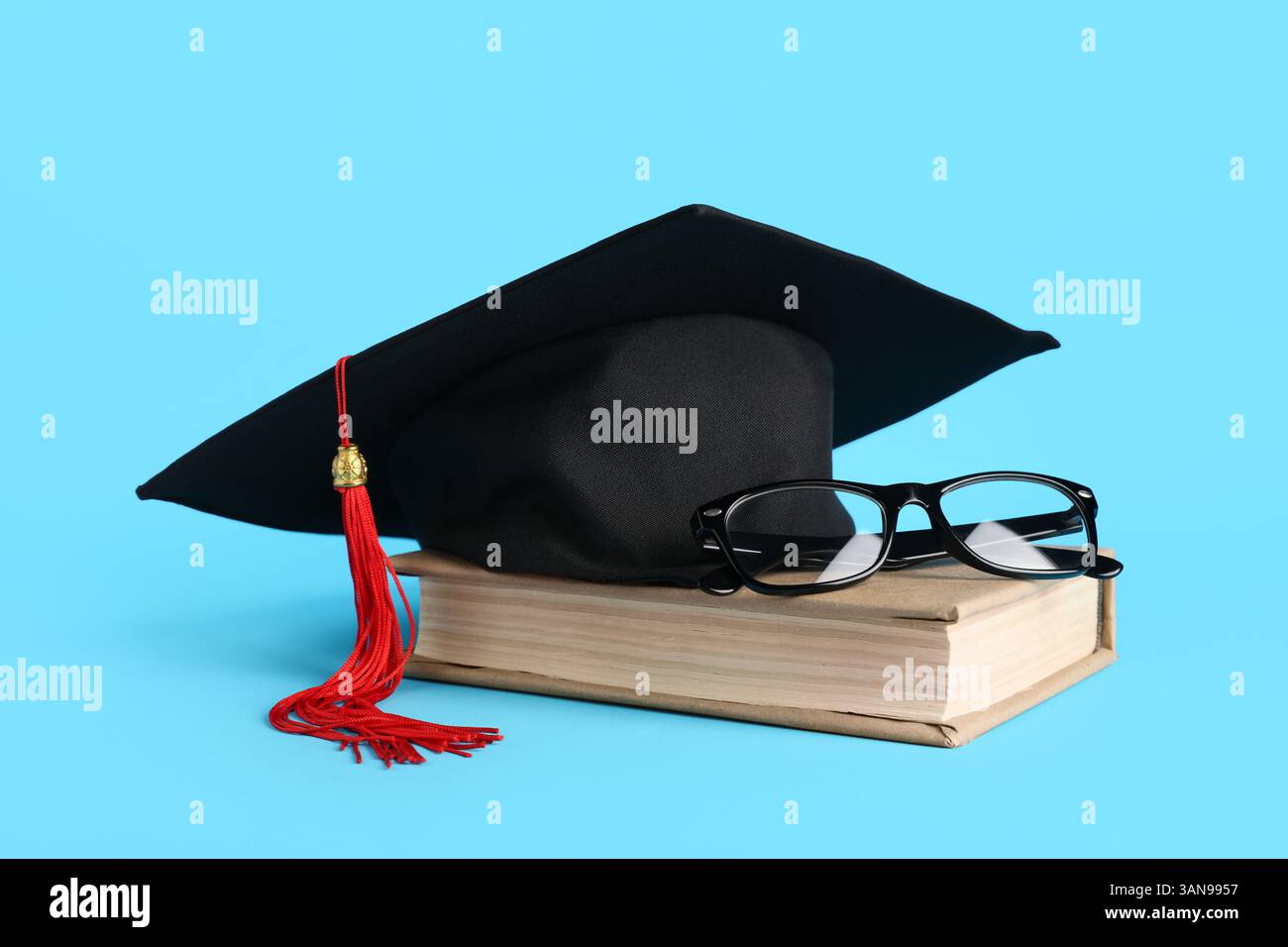 Cappello di graduazione, libro e occhiali su sfondo blu Foto Stock
