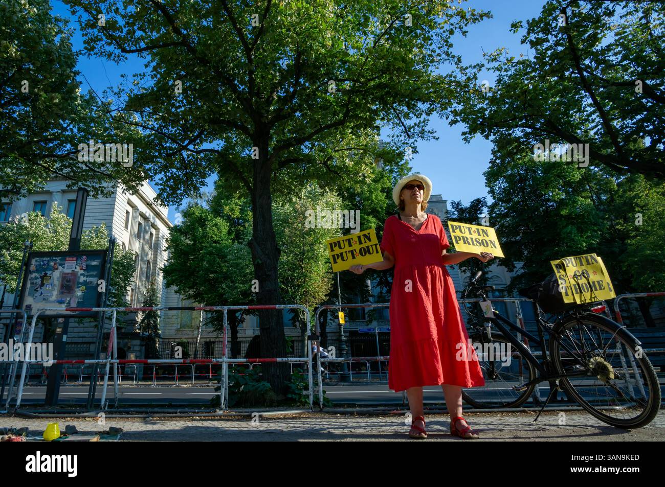 Una donna protesta di fronte all'ambasciata russa a Berlino, tenendo cartelli gialli con messaggi anti-Putin che chiedono giustizia e resistenza contro la guerra Foto Stock