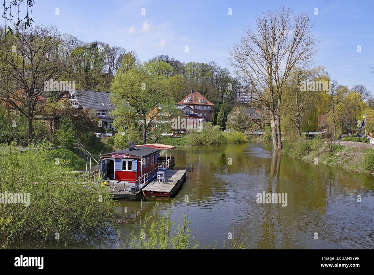 Fiume idilliaco con caffetteria boathouse, circondato da alberi sotto un cielo blu, primavera, Hitzacker, Elba, Wendland, bassa Sassonia, Germania, Europa Foto Stock