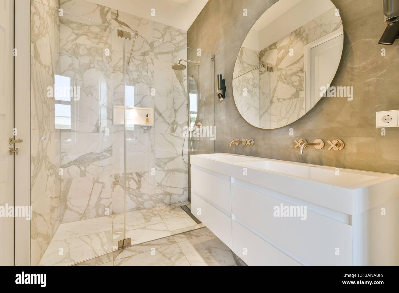 Un bagno elegante e moderno con eleganti pareti in marmo, un elegante specchio rotondo e mobili eleganti, che creano un'atmosfera sofisticata. Foto Stock