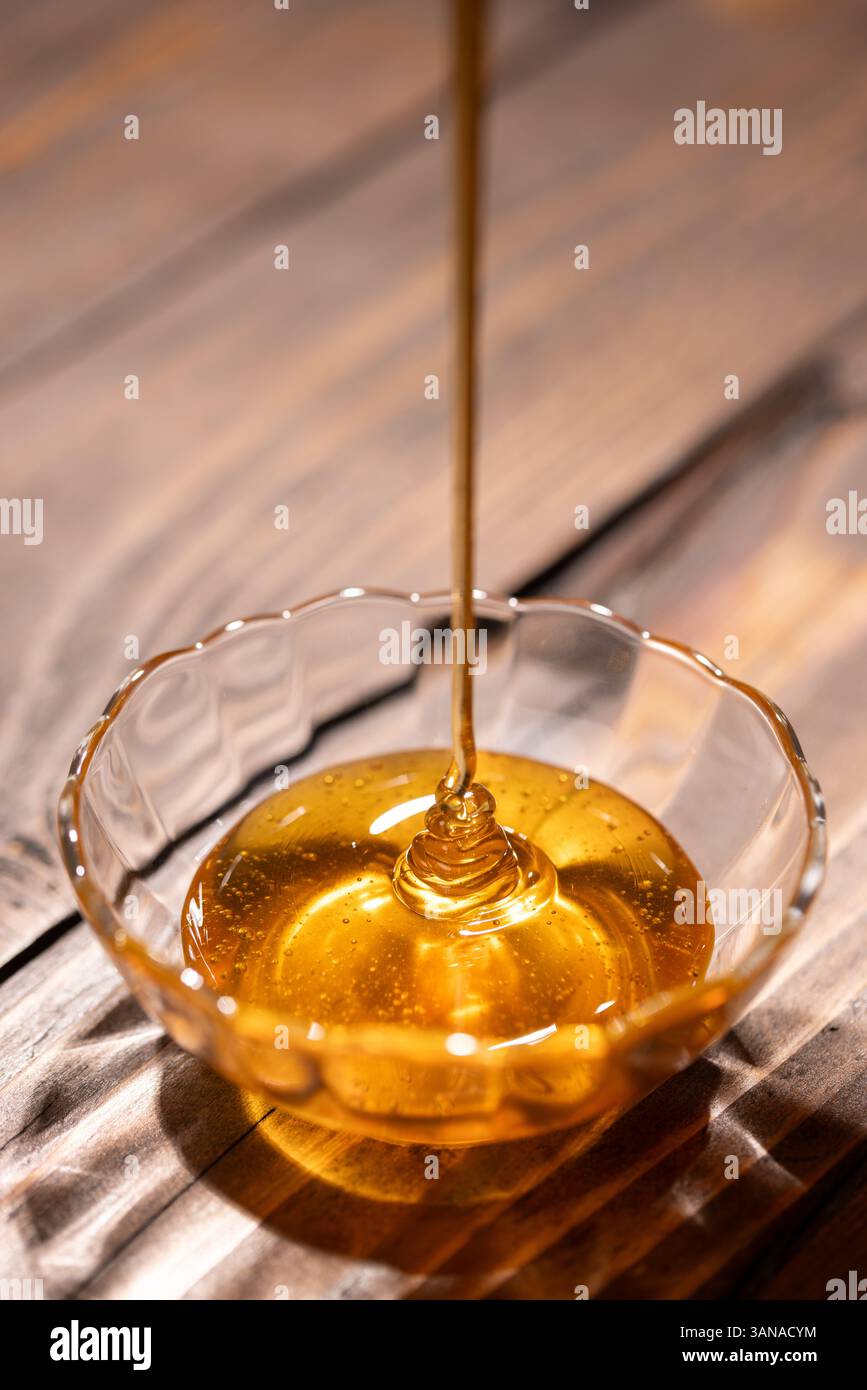 Il miele floreale fresco viene versato in un recipiente di vetro Foto Stock