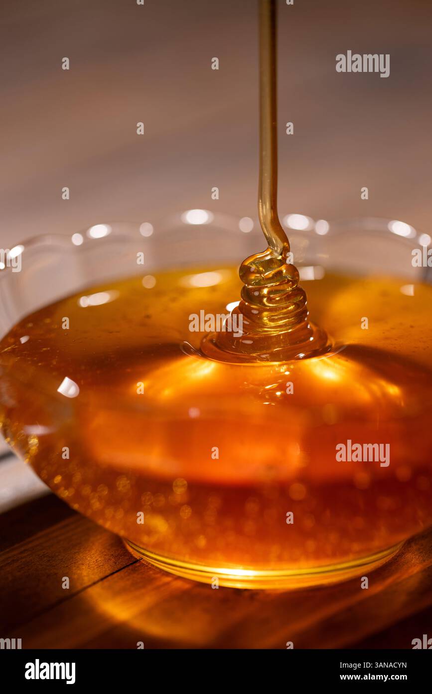 Il miele floreale fresco viene versato in un recipiente di vetro, primo piano Foto Stock