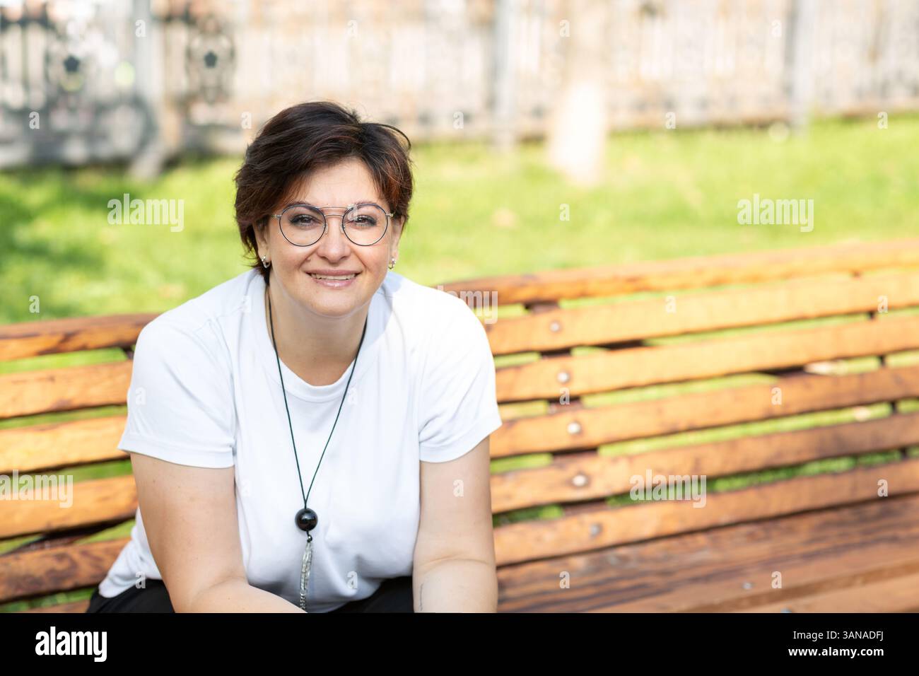 Una bella donna di mezza età con occhiali e capelli scuri corti è seduta su una panchina Foto Stock