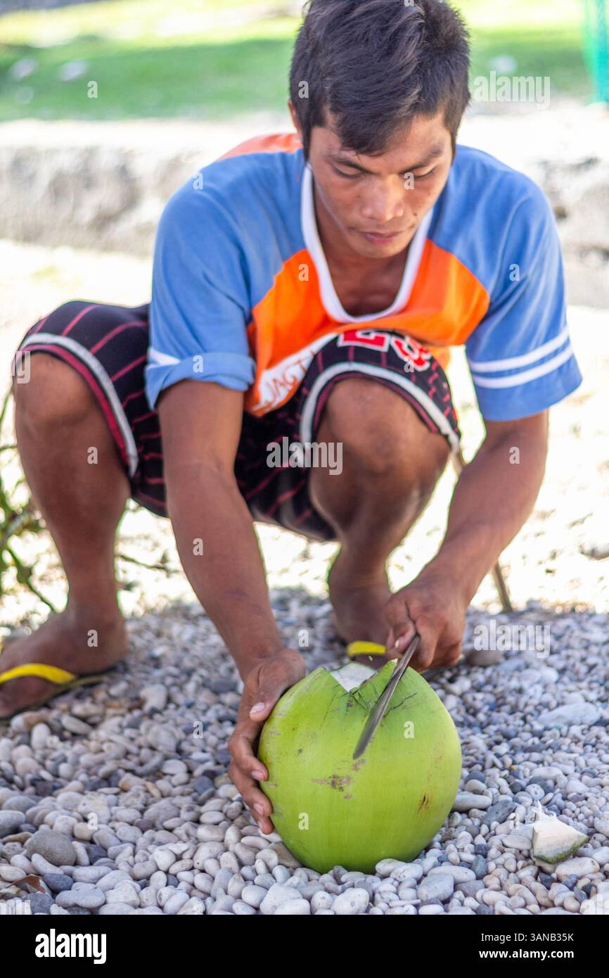 Un uomo filippino che hacking una noce di cocco verde per arrivare alla sua carne e all'acqua di cocco a Bicol, Filippine Foto Stock