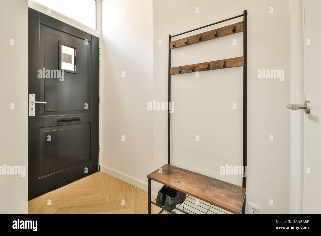 Un ingresso elegante e moderno con porta nera, appendiabiti in legno e pavimento elegante che mette in mostra elementi di design contemporanei. Foto Stock