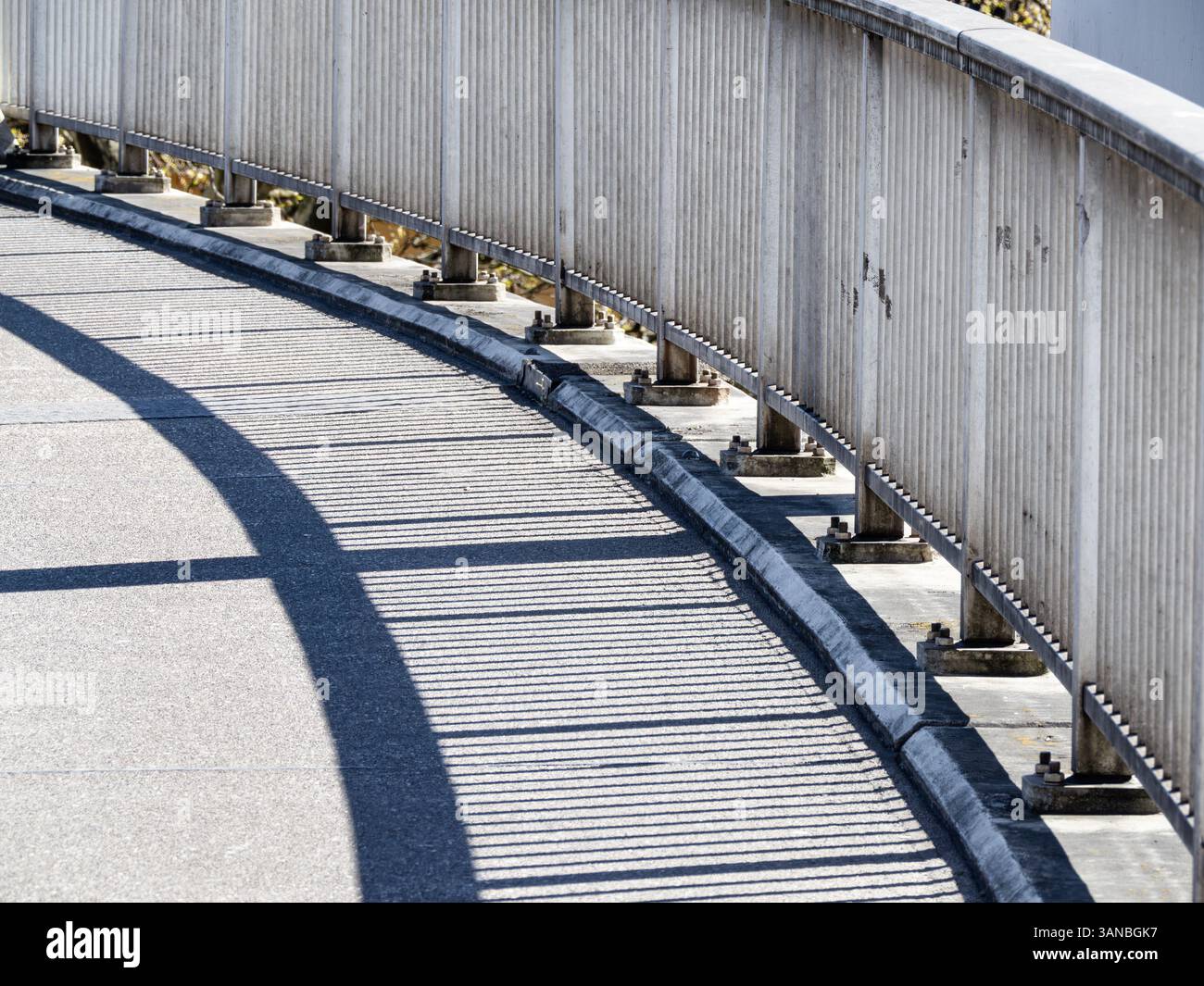 Passerella pedonale curva con ringhiera metallica che getta ombre sul terreno. Foto Stock