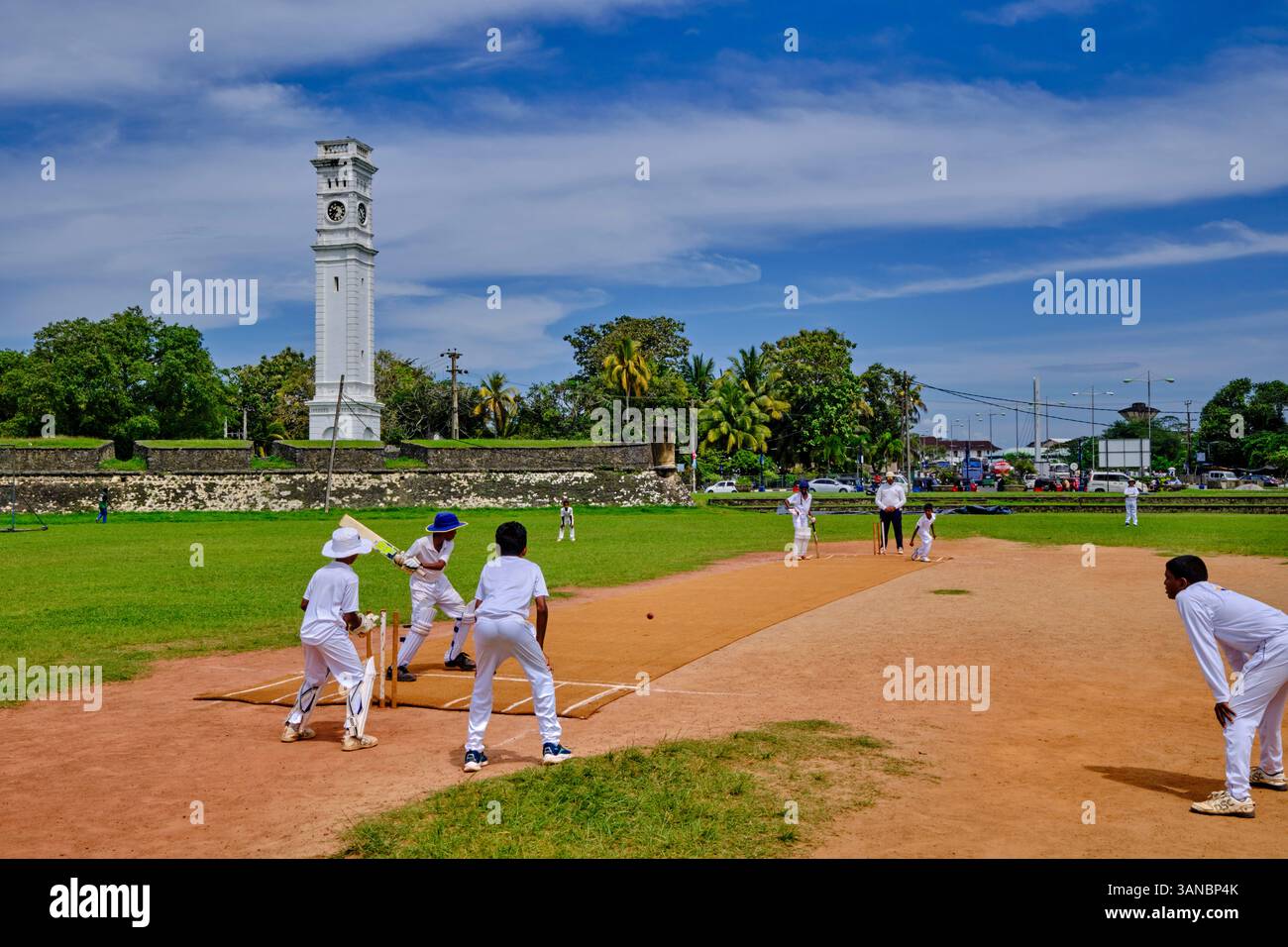 Sri Lanka, Provincia meridionale, Distretto di Matara, Matara, bambini che giocano a cricket di fronte alla torre dell'orologio di Matara Fort Foto Stock