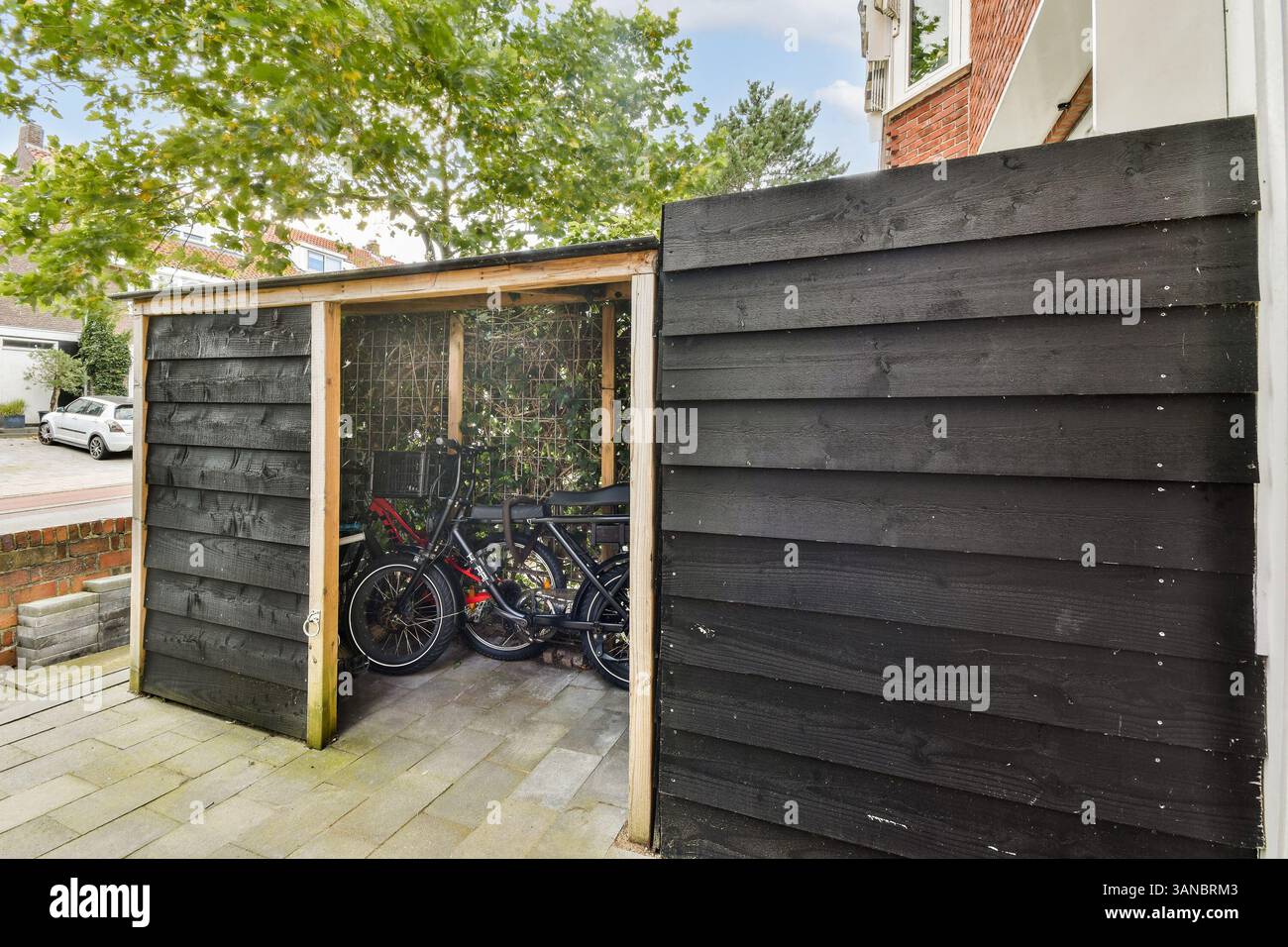 Un elegante capannone per biciclette realizzato in tavole di legno scuro, situato in un quartiere periferico con vegetazione sullo sfondo. Foto Stock