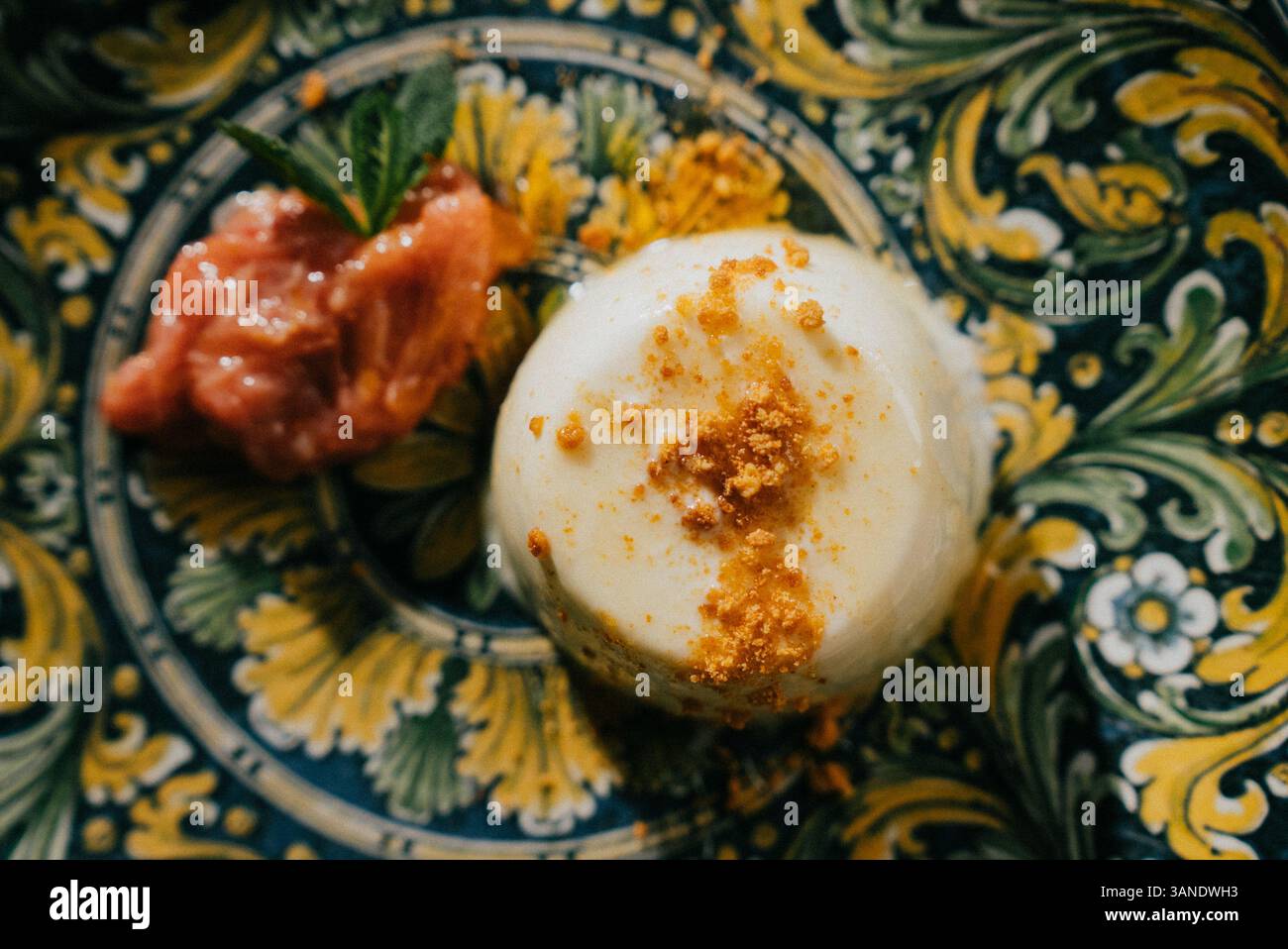 Un dessert con un condimento di noci tritate si trova su un piatto. Il dessert è una piccola torta con uno strato di marmellata sopra Foto Stock