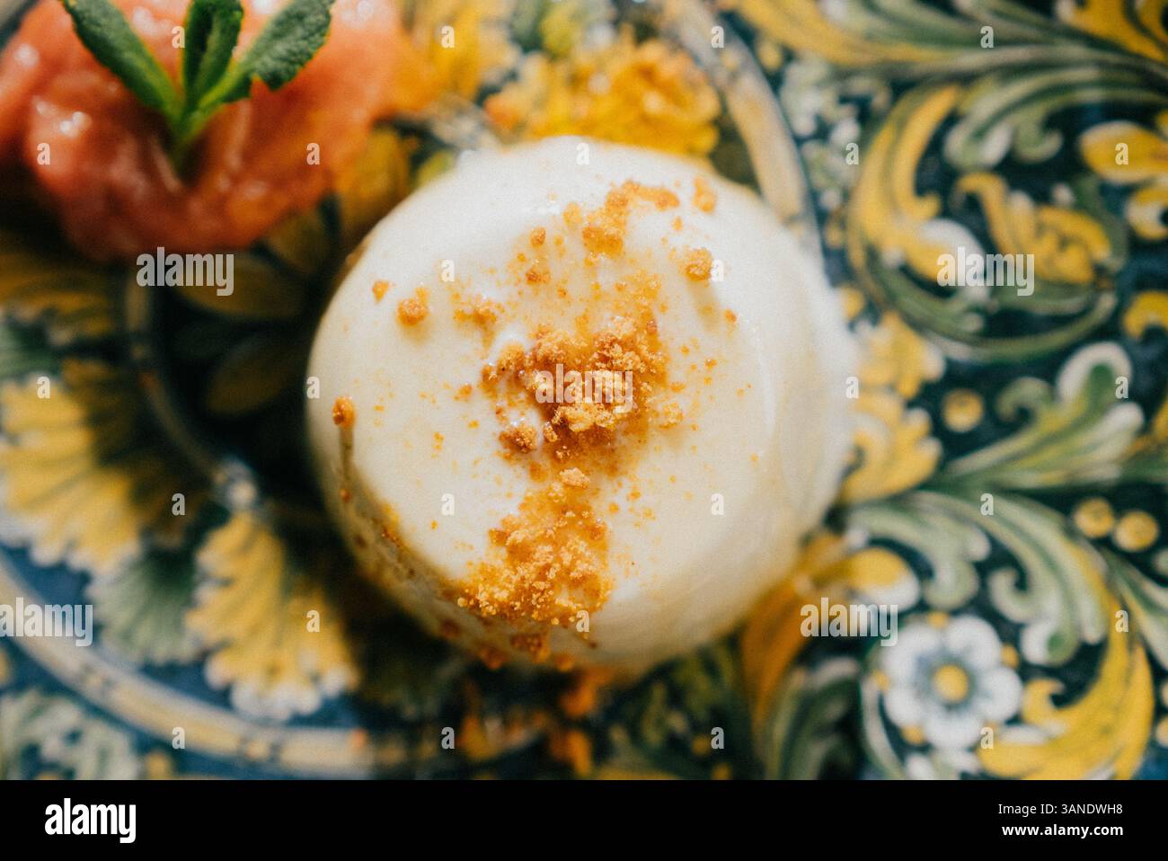 Un dessert con un condimento di noci e una fragola sopra. Il dessert è su un piatto dal design giallo e blu Foto Stock