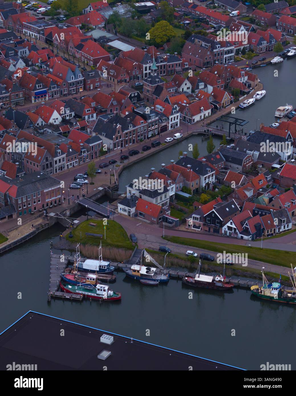 Vista aerea di un pittoresco villaggio con un affascinante porto e barche ormeggiate lungo un tranquillo canale, Makkum, Paesi Bassi. Foto Stock