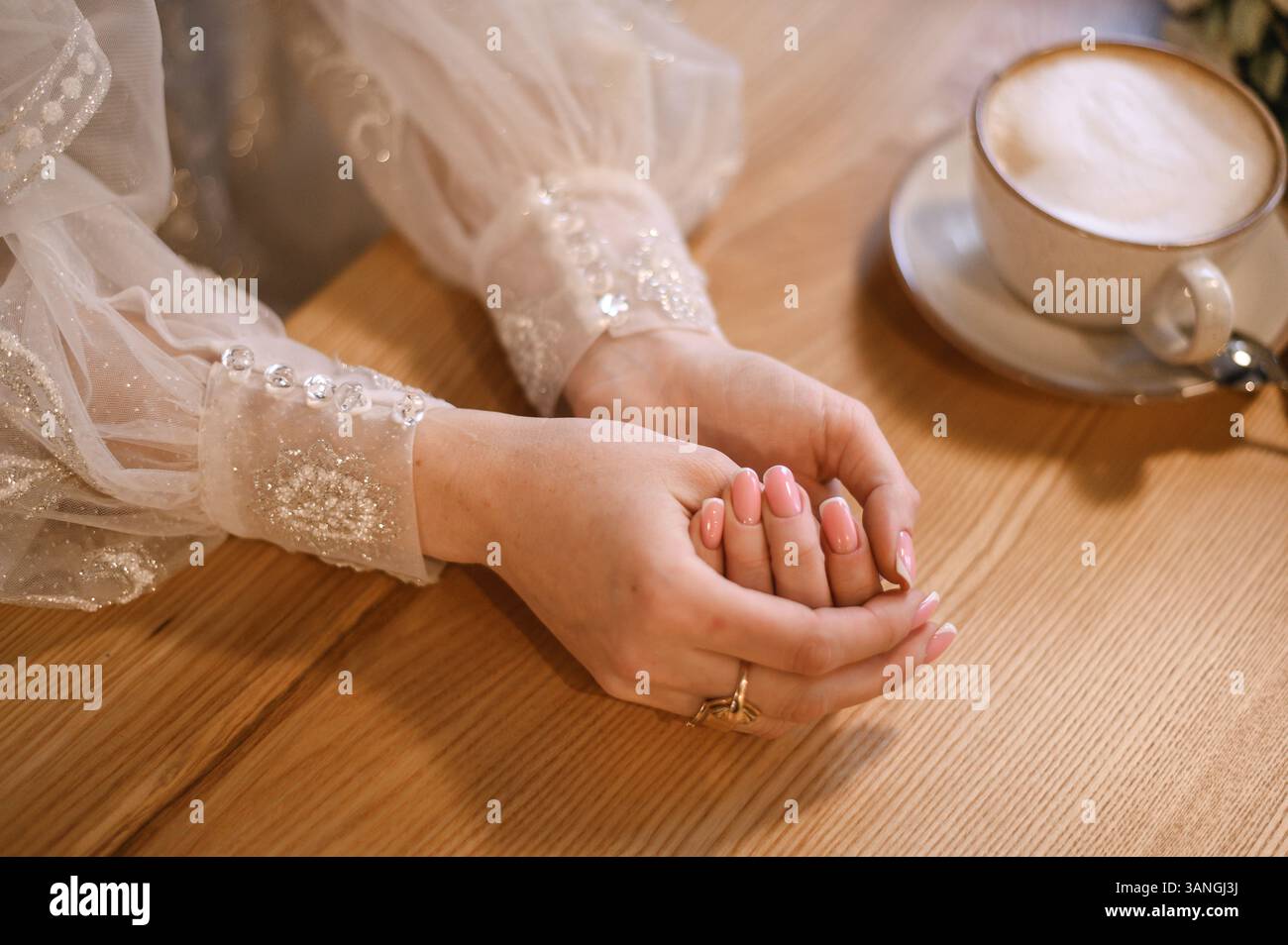 le mani di una donna su un tavolo in un bar e una tazza di cappuccino. Foto Stock