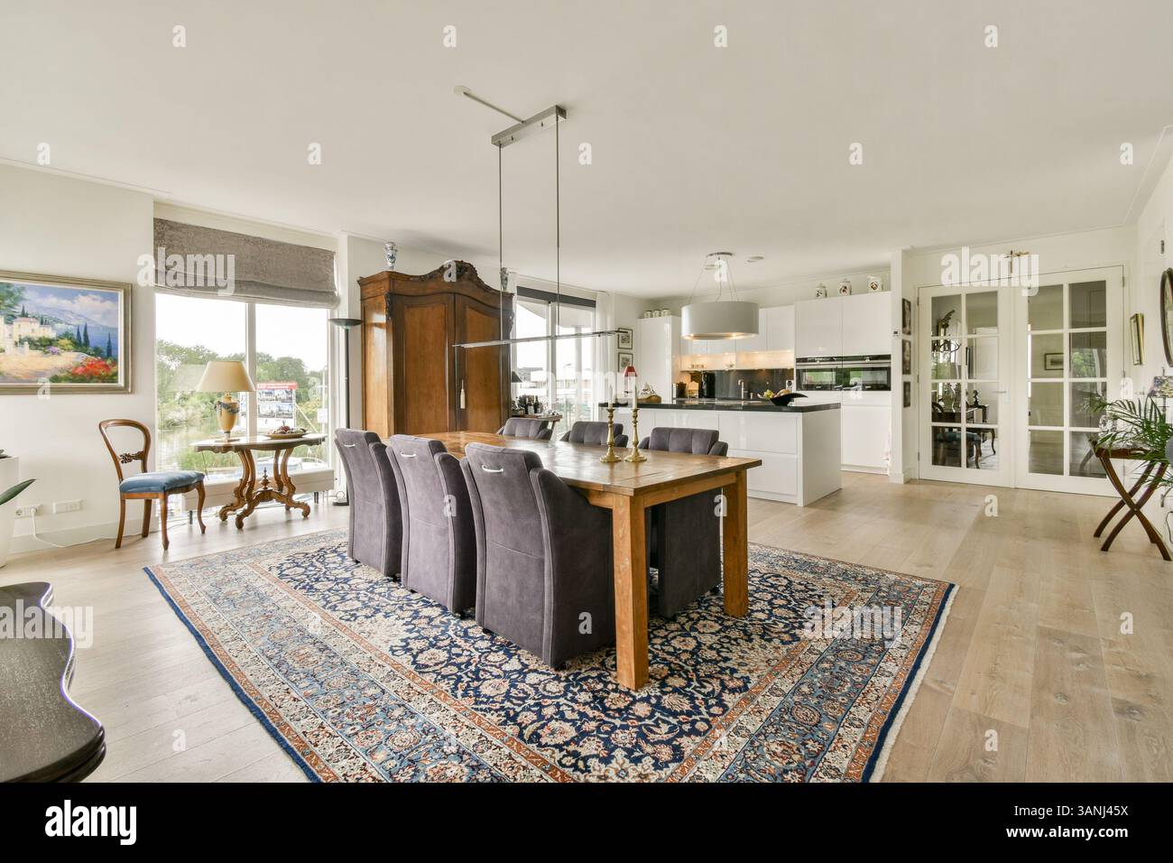 Un'elegante zona pranzo con tavolo in legno, sedie imbottite e grandi finestre che promuovono la luce naturale, completata da eleganti elementi di arredo. Foto Stock