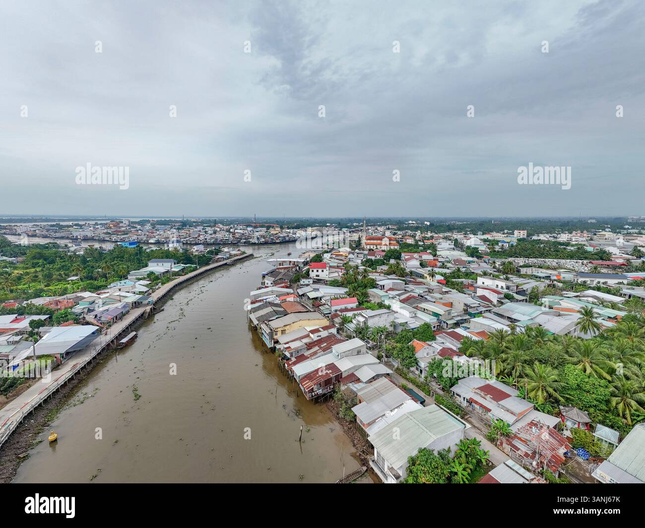 Vista aerea di una tranquilla area residenziale con tetti lungo un fiume panoramico e vegetazione lussureggiante, Dong Hoa Hiep, Tien Giang, Vietnam. Foto Stock