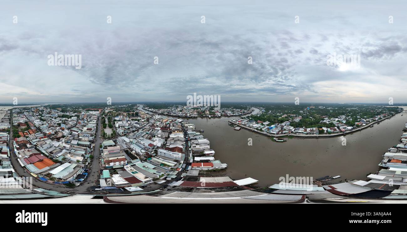 Vista aerea di un paesaggio urbano panoramico con case residenziali lungo un fiume sotto un cielo nuvoloso, Cai Be, Vietnam. Foto Stock