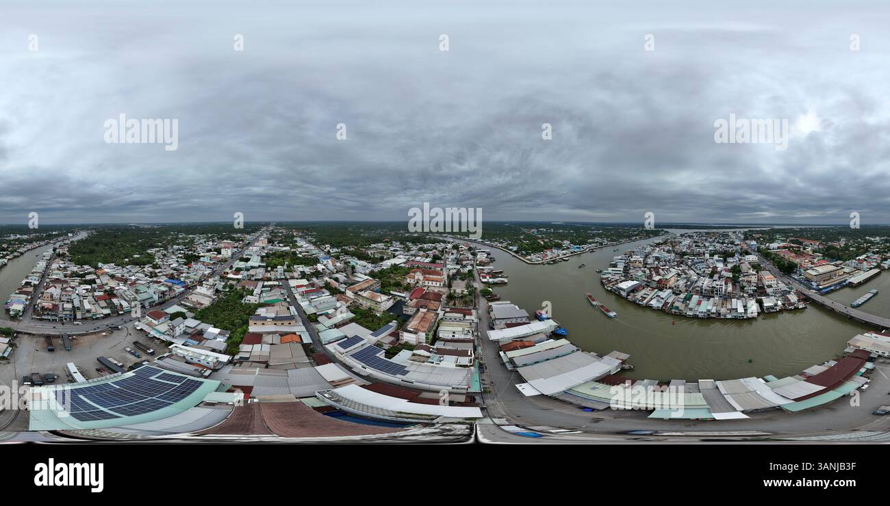 Veduta aerea di un paesaggio urbano lungo il fiume con edifici e tetti sotto un cielo nuvoloso, Cai Be, Vietnam. Foto Stock
