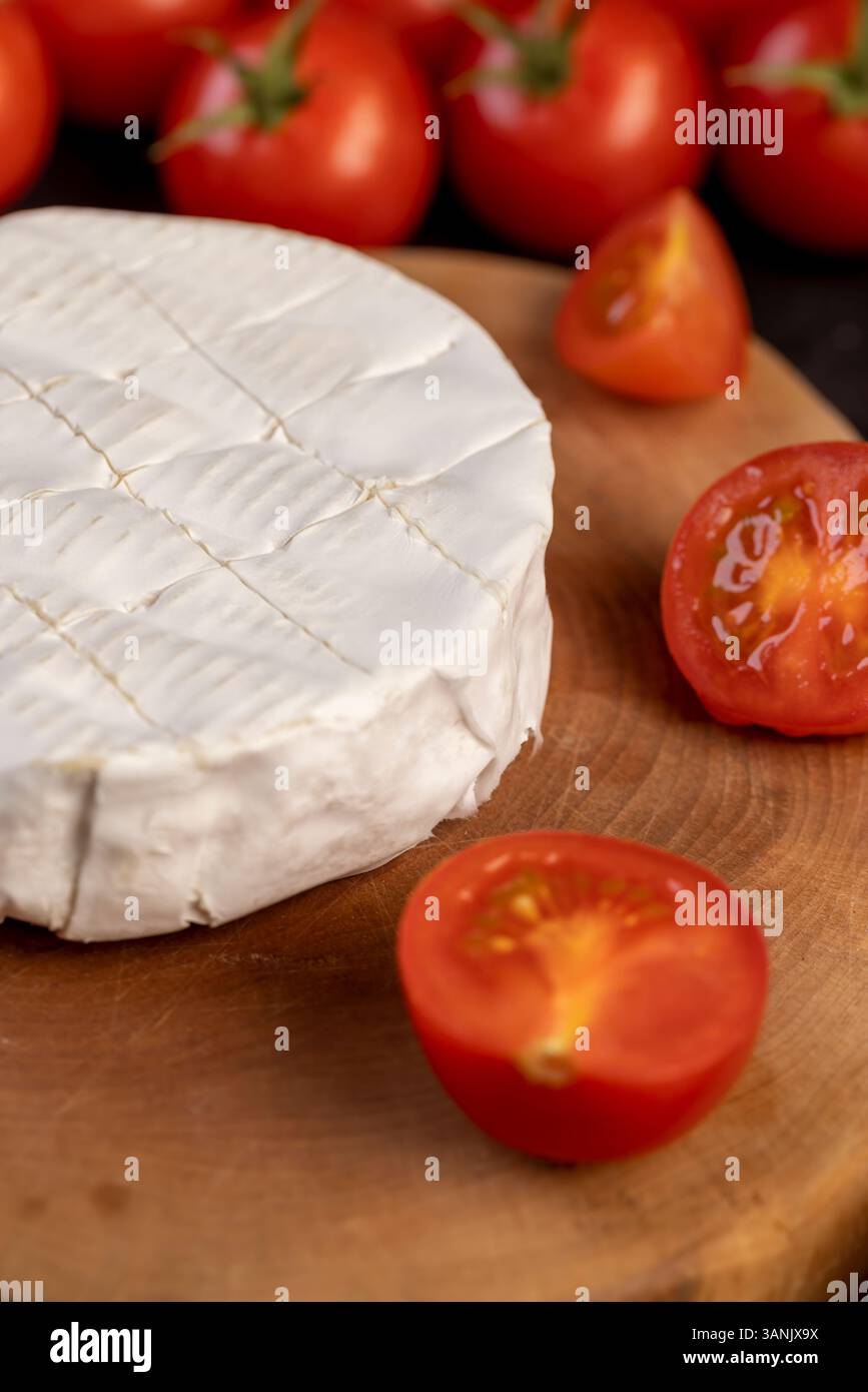 formaggio con muffa e pomodori, un pezzo di formaggio morbido maturo e alcuni piccoli pomodori rotondi rossi sul tavolo Foto Stock