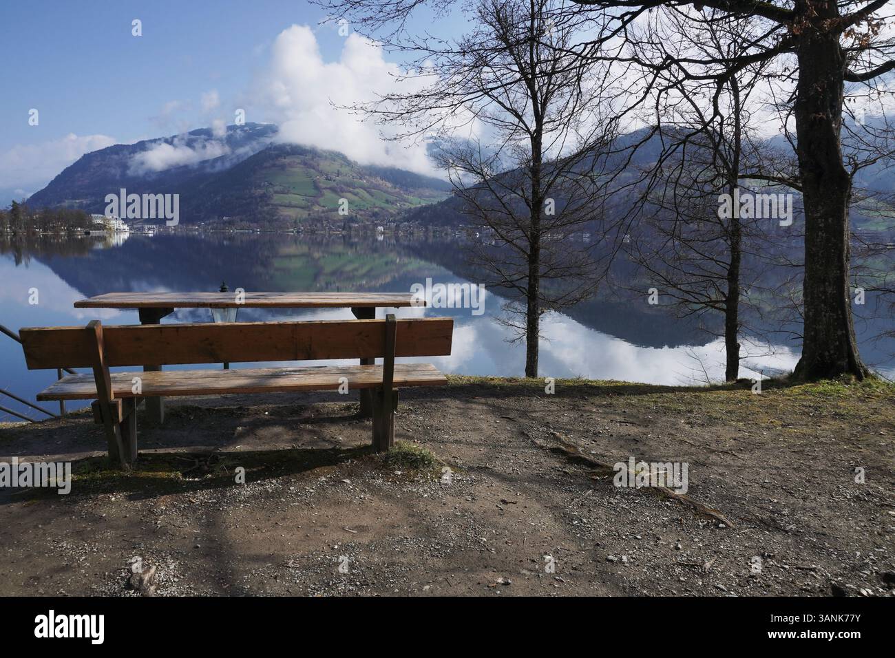 La panchina e il tavolo in legno con vista, giornata di tempo nuvoloso di Zell am SEE, situato nelle Alpi austriache. montagne e città sullo sfondo, che si rispecchiano Foto Stock
