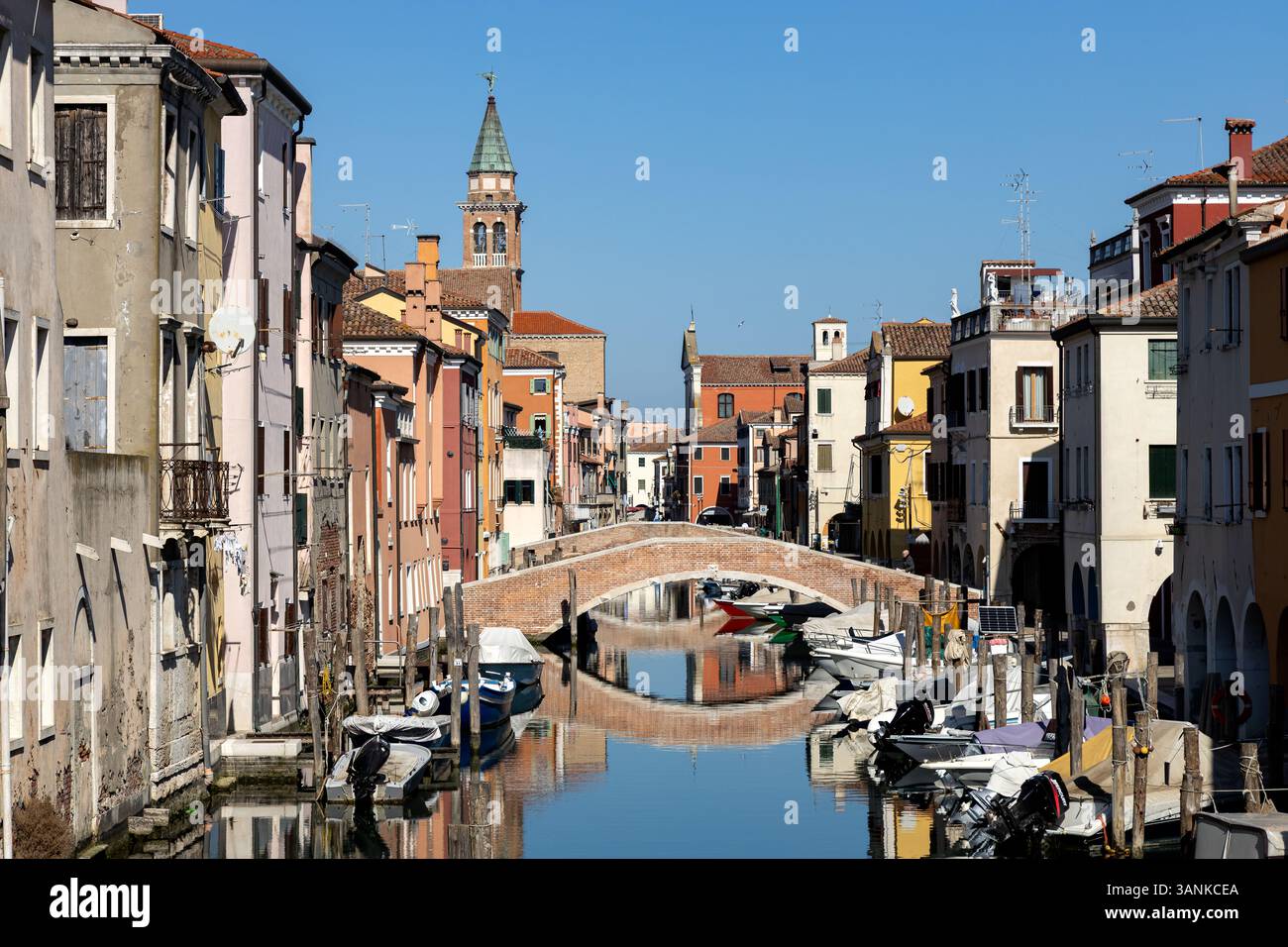 Chioggia, Italia - 3 marzo 2025: Veduta del Canal Vena con barche ormeggiate, un ponte pedonale e riflessi nel centro storico della città Foto Stock